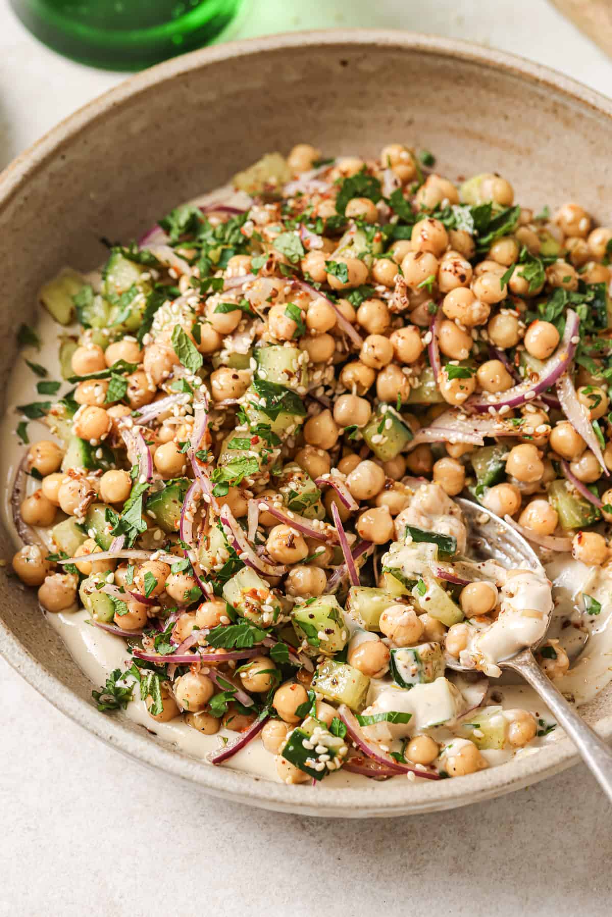 Angled overhead shot of chickpea salad in a beige bowl with a spoon.