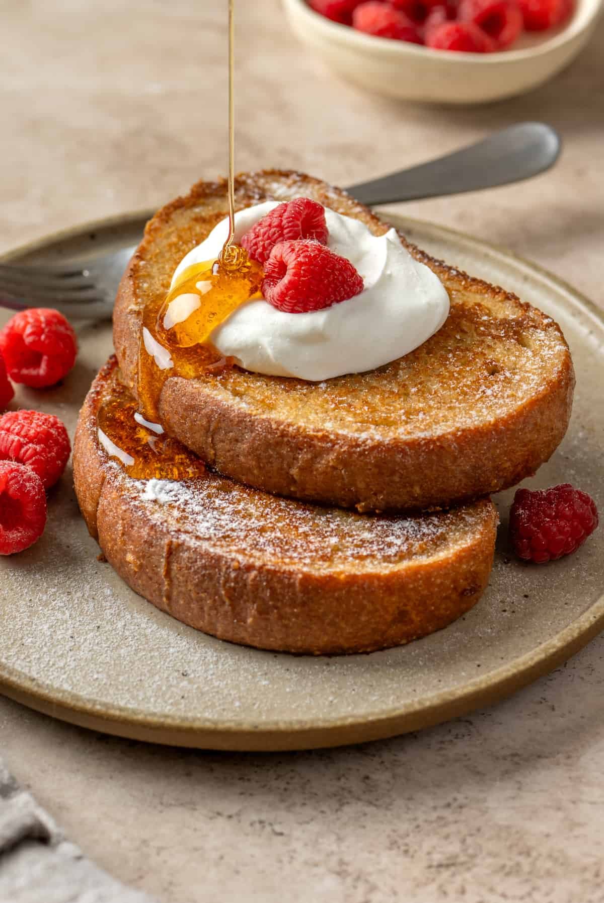 Side view of someone pouring maple syrup on two slices of vegan french toast.