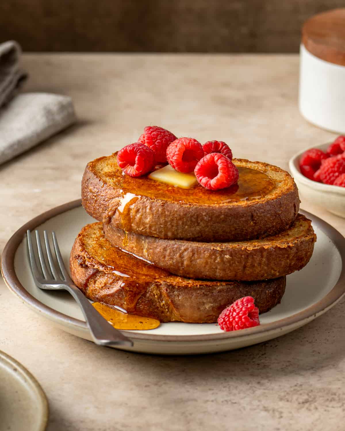 Side view of vegan french toast with butter and raspberries.