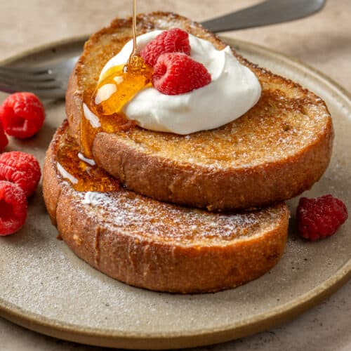 Side view of someone pouring maple syrup on two slices of vegan french toast.