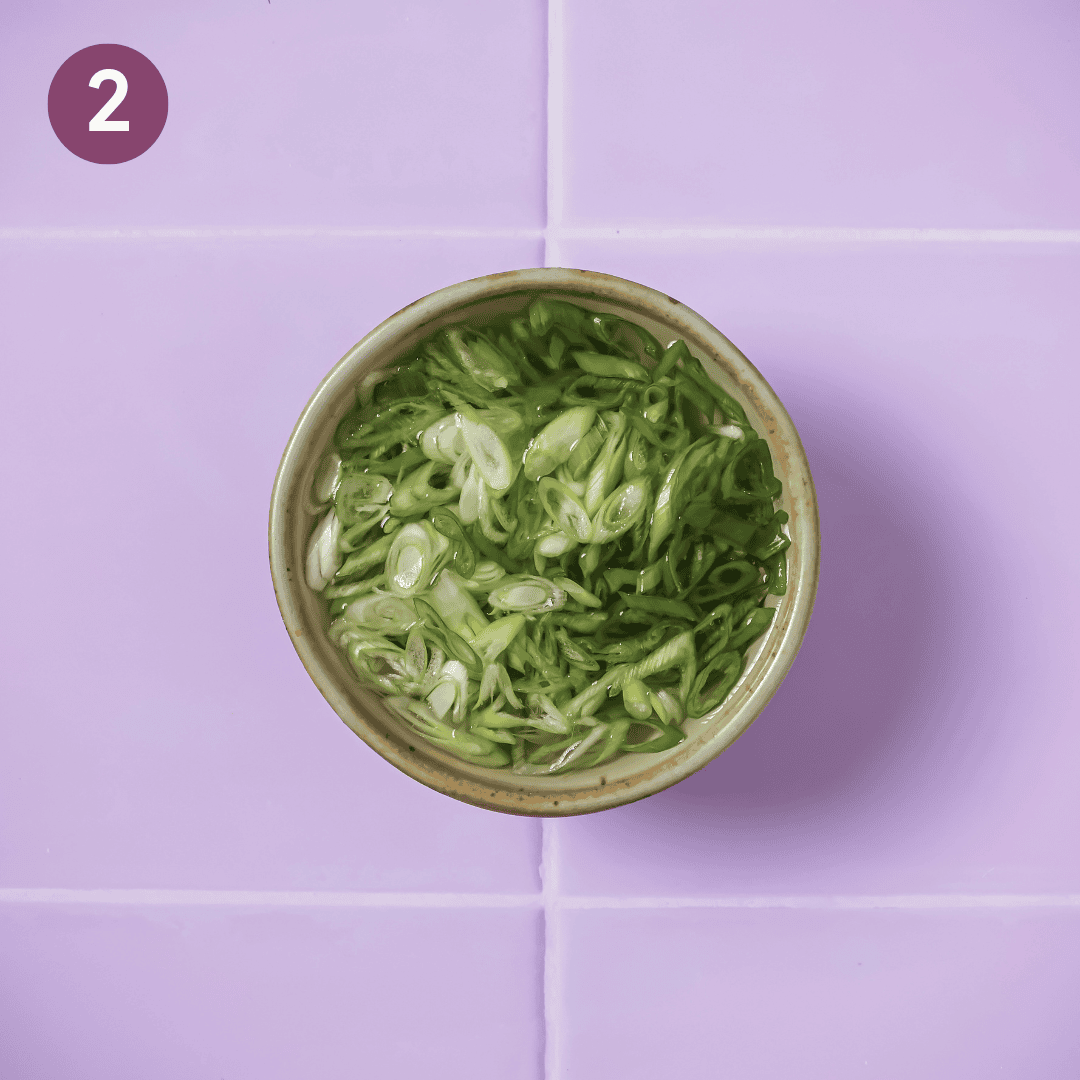 sliced scallions soaking in a small bowl of ice water.