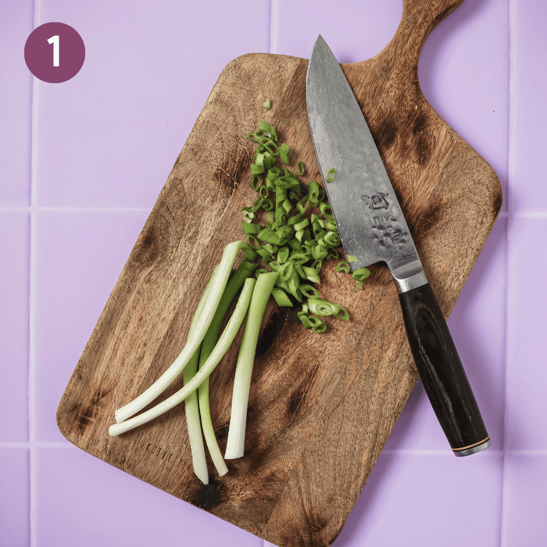 scallions sliced on a bias and a knife on a wooden cutting board.