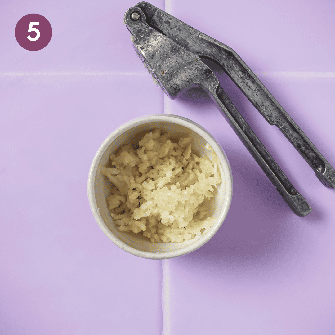 a bowl of minced garlic next to a garlic press on a table.