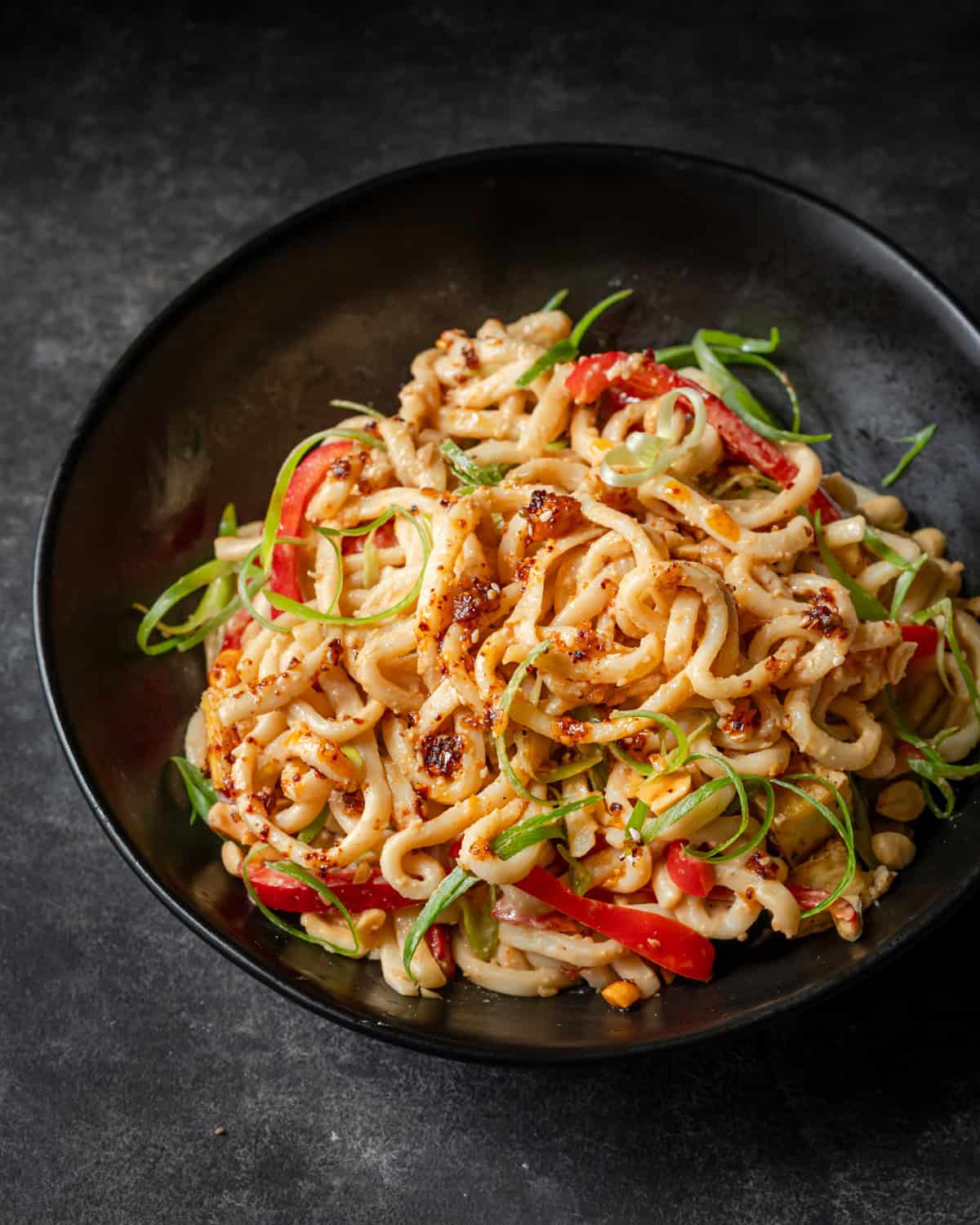 Peanut noodles with red peppers, green onions, tofu, and peanuts, drizzled with chili oil.