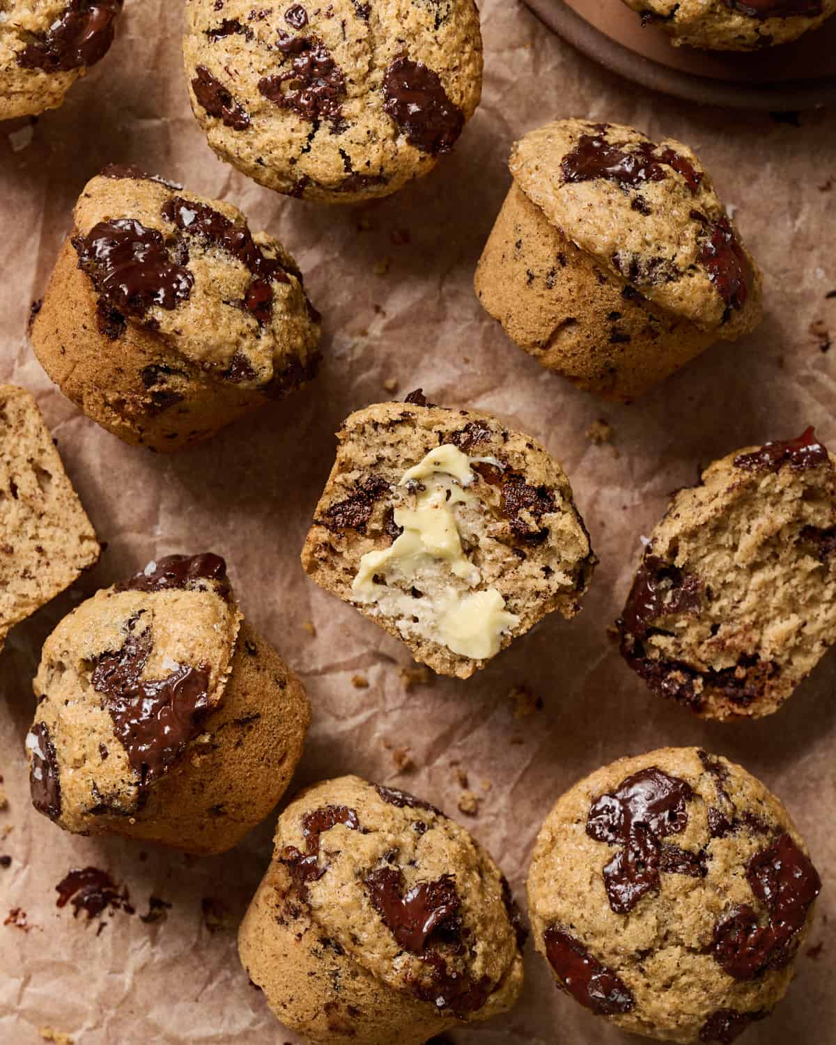 Overhead view of muffins on parchment paper, one is cut in half with butter on it.