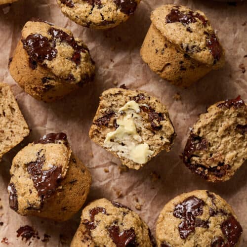 Overhead view of muffins on parchment paper, one is cut in half with butter on it.