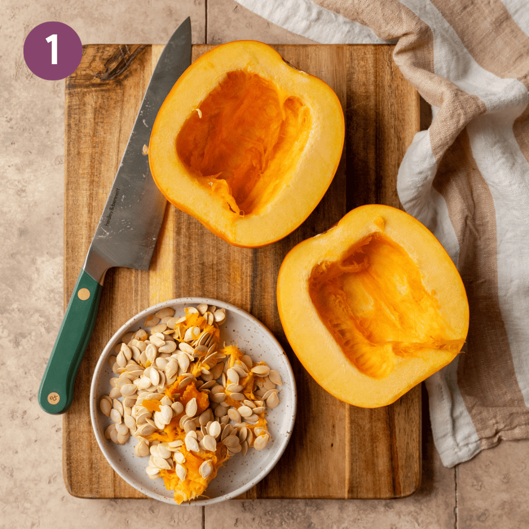 Two pumpkin halves and a knife on a wooden cutting board.
