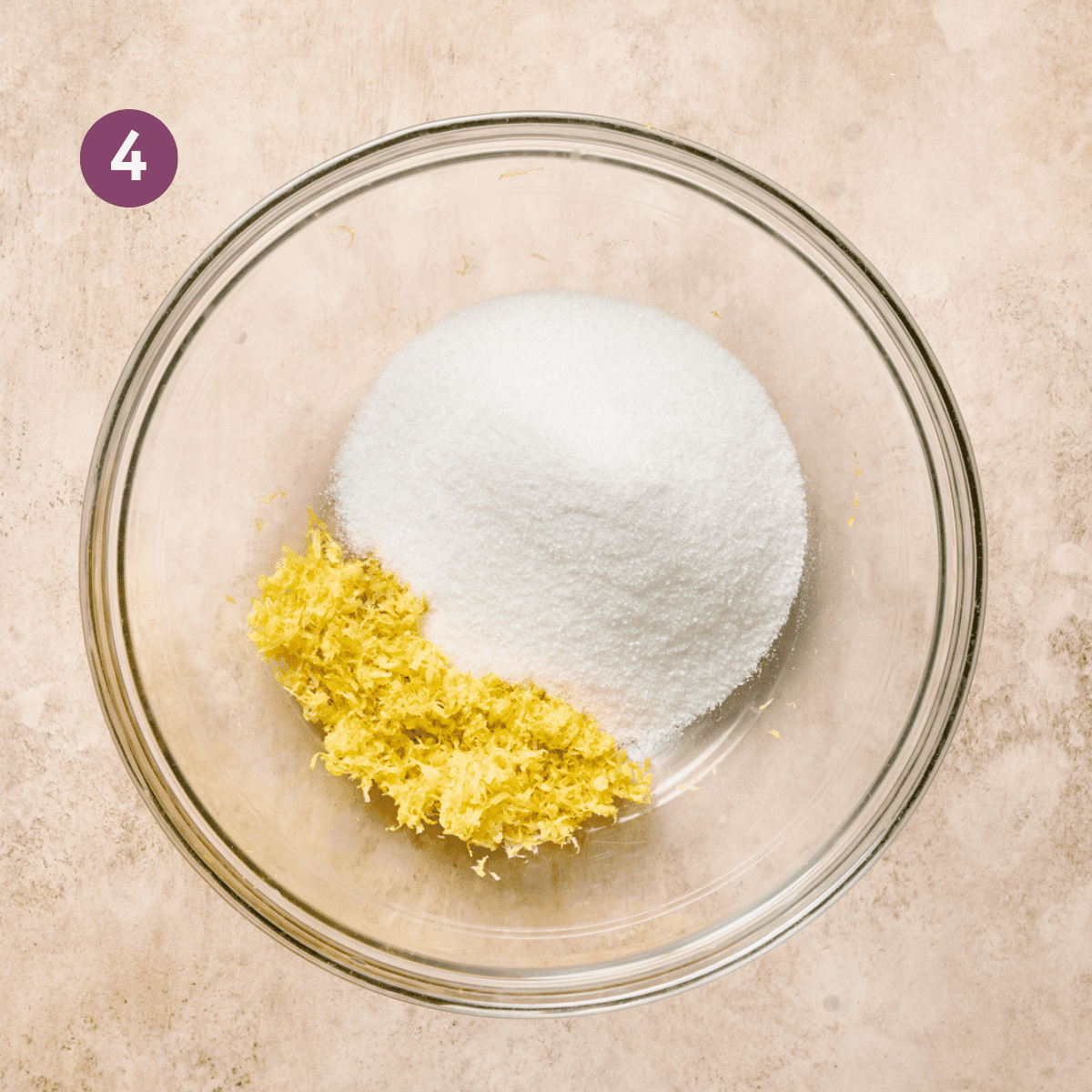 sugar and lemon zest in a large glass bowl on a light pink surface.