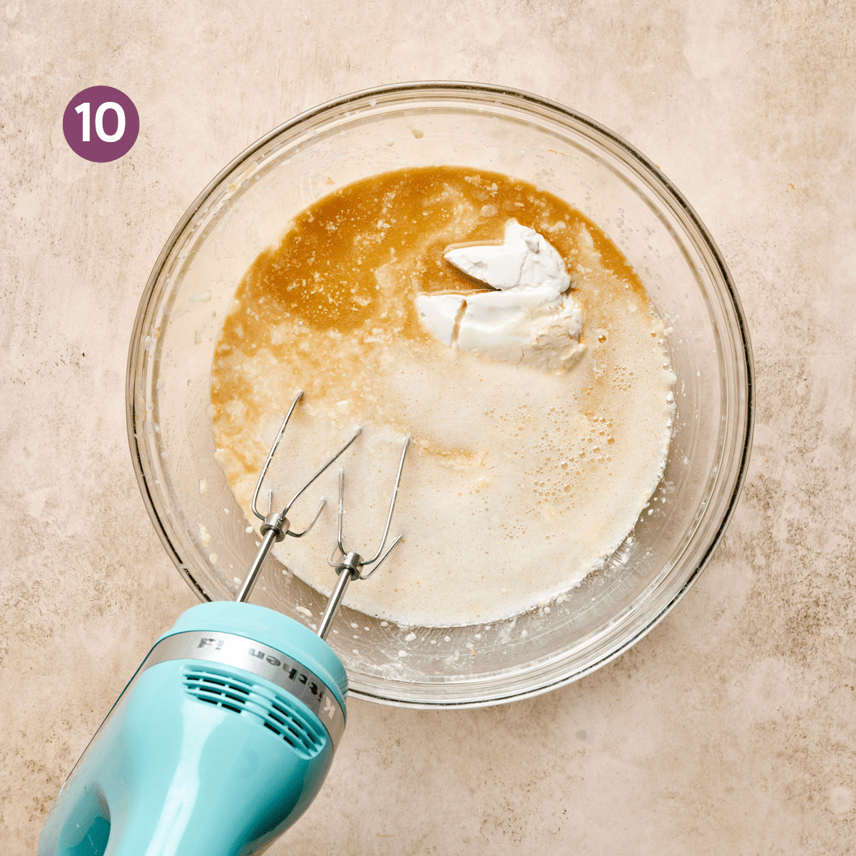 light blue electric mixer in a glass bowl of vegan sour cream, milk, sugar, butter, and vanilla.
