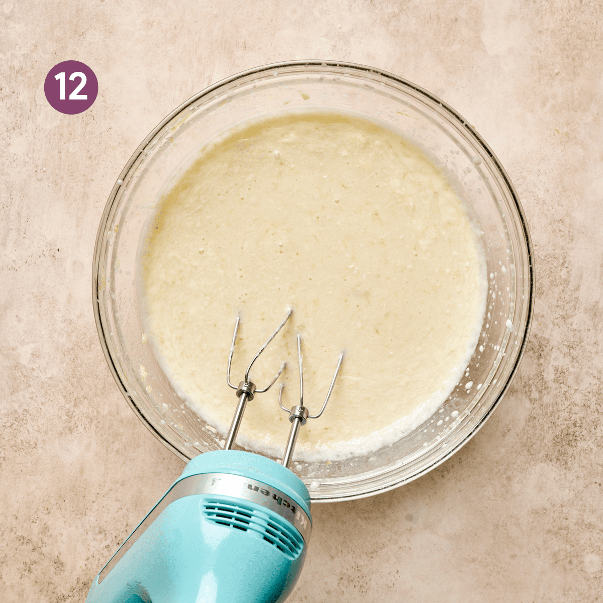 finished texture of mixed liquid ingredients in a glass bowl with a light blue electric mixer.