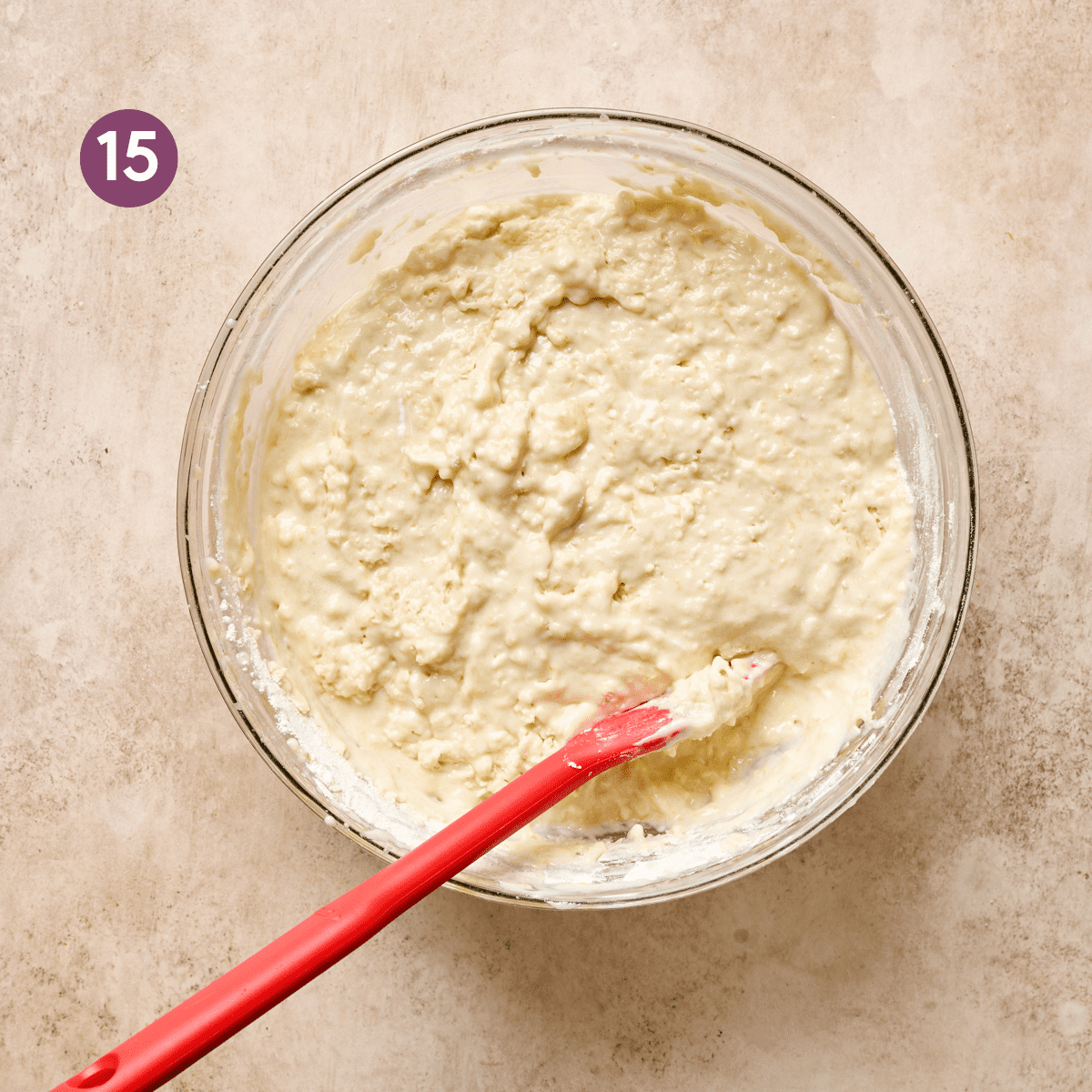 final texture of vegan lemon cake batter in a glass bowl with a silicone spatula in the bowl.