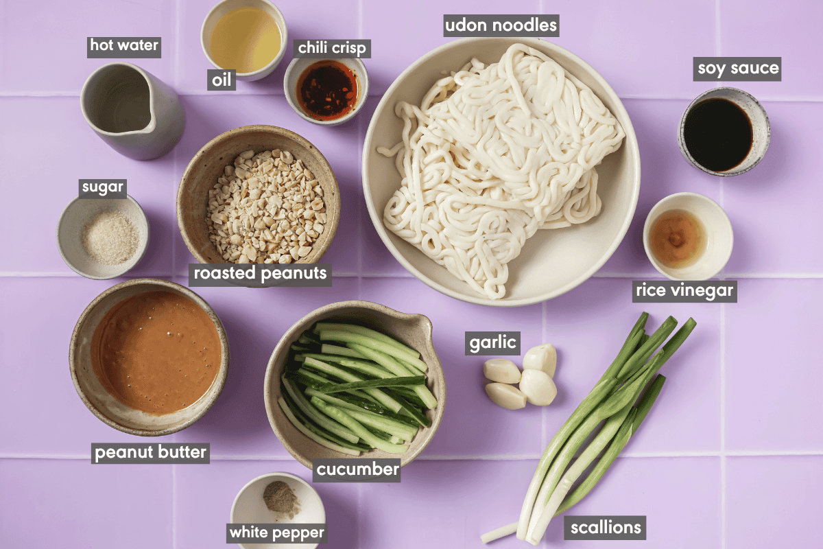 various ingredients for peanut noodles in bowls on a tiled surface.