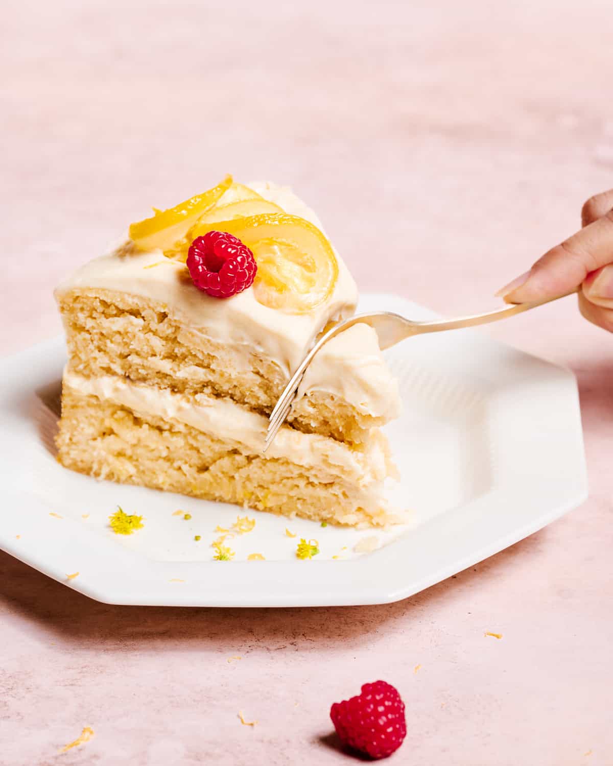 two-layer vegan lemon cake with lemon cream cheese frosting on a white cake stand topped with candied lemons.
