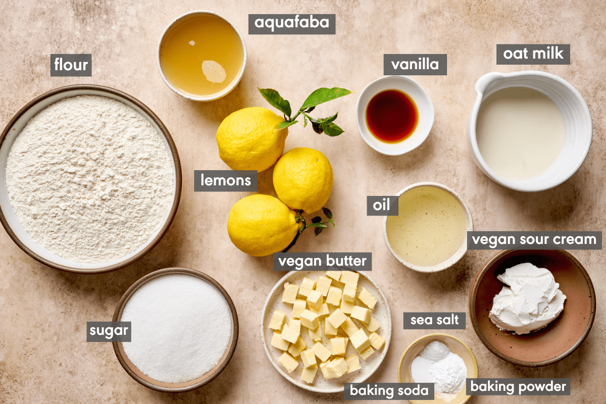 ingredients for vegan lemon cake laid out on a light pink surface with ingredients labeled.