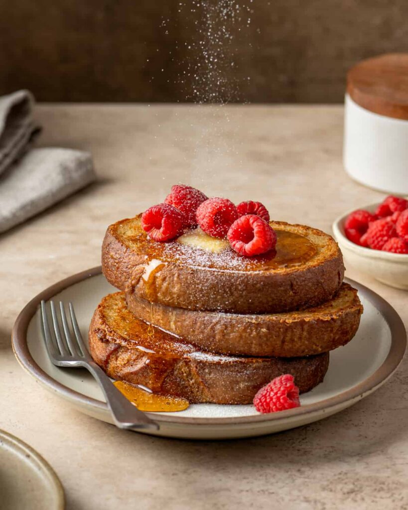 Side view of someone pouring maple syrup on two slices of vegan french toast.